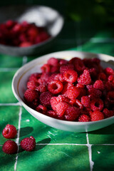 Plate of freshly picked red raspberries on green tile background. Concept of vibrant colors, summer, harvest, healthy organic food.