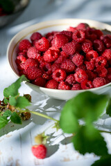 Plate of freshly picked raspberries on white wooden background. Concept of harvest, healthy organic food, summer berries.