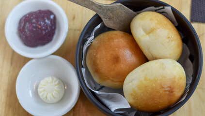 Bread rolls served warm in a black bowl, paired with purple berry jam and creamy butter. Their golden, glossy crust and soft texture make them perfect for breakfast, brunch, or a cozy snack.