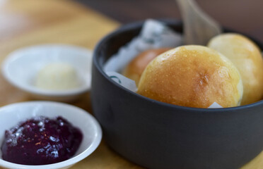Bread rolls served warm in a black bowl, paired with purple berry jam and creamy butter. Their golden, glossy crust and soft texture make them perfect for breakfast, brunch, or a cozy snack.
