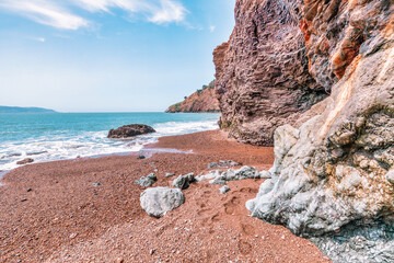 Kirby Cove Beach in California with red sand, blue ocean waves, and dramatic cliffs covered in pine...