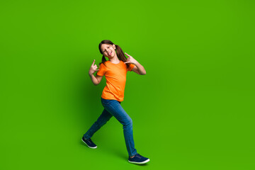 Happy young girl in orange t-shirt displaying playful gestures against vibrant green background, representing carefree childhood.