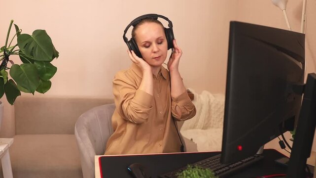 A focused young white woman on a computer at her desk. She's wearing headphones. Listening to music.