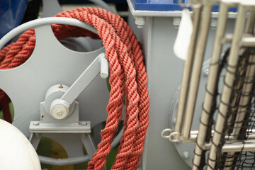 Marine winch with red braided rope on grey metal reel showing functional nautical hardware for industrial and maritime use.