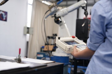 Engineer is using remote to control production process of modern robotic arm machine in automotive industry.