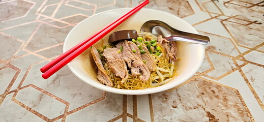 Duck noodles without soup served in white cup with spoon and red chopsticks. Dry egg noodles with...