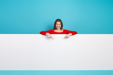 Young woman in red top smiling and pointing to a blank white board space against a vibrant blue...