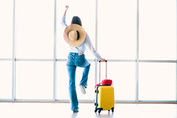 Young woman in casual summer outfit at airport with suitcase, expressing joy of travel, ready for...