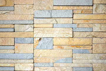 A wall composed of rough-textured natural stone with dominant colors of dark gray, black, and...