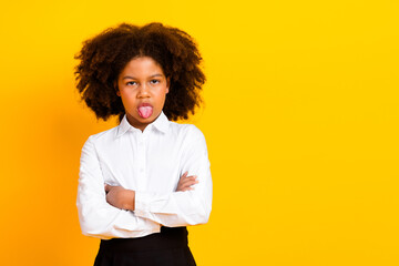 Confident schoolgirl showing playful expression in formal attire on a vibrant yellow background...