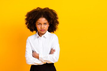 Confident schoolgirl with folded arms against bright yellow background in formal attire symbolizing...