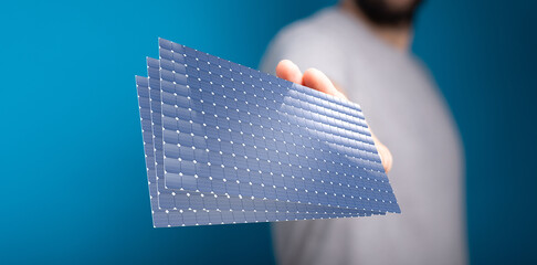 Image of a person holding a stack of solar panels. Clean energy, renewable energy, sustainability.