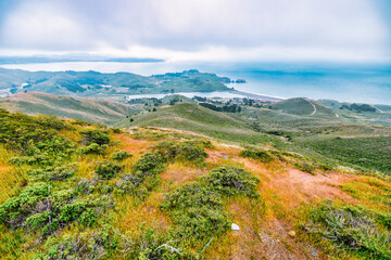 Winding trail through the lush, green hills of Marin Headlands near Rodeo Beach, overlooking the Pacific Ocean under dramatic coastal skies in Northern California.