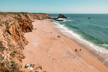 Panther Beach in California with turquoise waves, golden sand, and dramatic cliffs, seen from above...