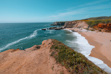Panther Beach in California with turquoise waves, golden sand, and dramatic cliffs, seen from above near scenic Highway 1 on a clear spring day