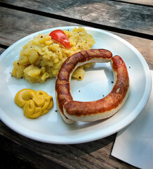 Typical Bavarian food in beer garden: pork grilled sausage ( Bratwurst) with potato salad and mustard served on a rustic wooden table outdoors