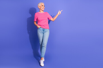 Confident Woman in Colorful Fashion Pointing Upwards on Purple Background, Expressing Cheerfulness...