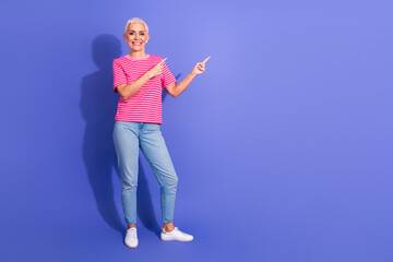 Confident mature woman in casual summer outfit gesturing and promoting with bright smile against purple background