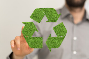 Eco-friendly concept image. Person interacts with a recycling symbol made of green grass.