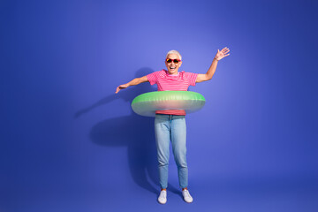 Elderly woman enjoying leisure wearing stylish casual outfit with inflatable ring on vibrant purple...
