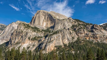 A natural scene showing a contrast between light and red granite rocks surrounded by green trees and a vibrant blue sky.