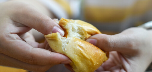 Bread being gently torn apart by two hands, revealing its soft, fluffy interior. The close-up captures warmth, freshness, and a shared moment of enjoying freshly baked goods.