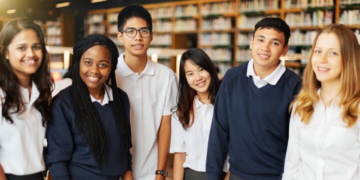 Group of diverse students in uniform in school library work on group project. Diverse students work together on group project in library. High school education photo, group of happy diverse students