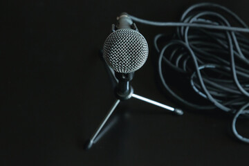 A microphone stands on a special microphone stand on a black table surface next to a coiled black...