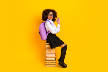 Cute schoolgirl with curly hair smiling on books in front of yellow background, conveying education and youthfulness