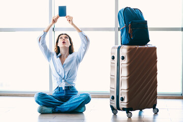 Passenger Woman Sitting at Airport Terminal with Suitcase and Holding Travel Document in...