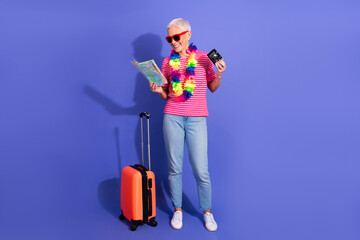 Fashionable elderly woman with luggage and map exudes joy and travel spirit on a vibrant purple...