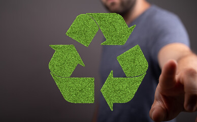 Eco-friendly concept image. Man points to a green recycling symbol made of grass.