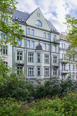 Fototapeta premium Elegant historic residential building in Prague, Czech Republic, framed by blooming lilac bushes and spring greenery, showcasing beautiful European architecture and ornate window details.