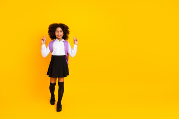 Cheerful schoolgirl with a stylish uniform and backpack against a vibrant yellow background,...