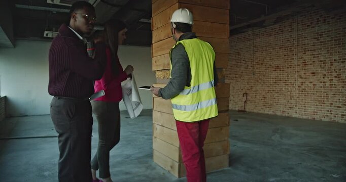 A multinational business team discusses construction plans in a new office space. The team collaborates, demonstrating teamwork and planning during a renovation or building project.