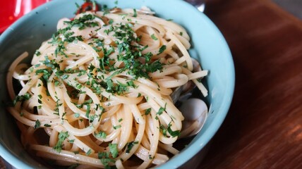 close up of spaghetti alle vongole with clams and herbs in a light blue plate on a wooden table with copy space