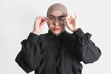 Confident woman in hijab adjusting her glasses with a focused look on isolated on white background. 