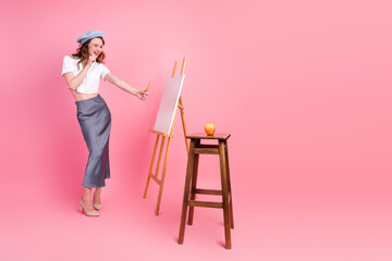 Youthful woman artist sketching on a canvas with a playful demeanor in a pink studio setting with...