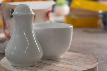 Minimalist white salt shaker and bowl on textured countertop. Ideal for modern kitchen, food styling background, or product presentation.