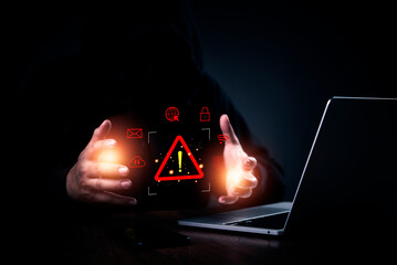 hacker in a hoodie with hands protecting a glowing warning icon. Cybersecurity, data breach, and...