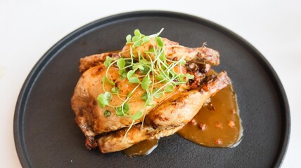 close up of dish of roasted golden-brown chicken with crispy skin.  Garnished with fresh microgreens on top and with savory sauce with copy space