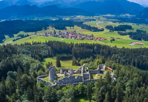 Aerial view of the striking ruins of Eisenberg Castle amidst a sea of green forest and rolling hills, framed by distant mountains, Eisenberg, Bavaria, Germany.