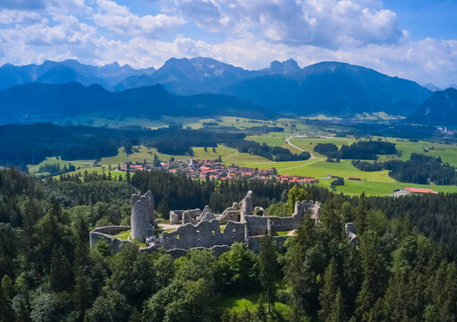 Aerial view of the ancient castle ruins surrounded by emerald forests, contrasting with the distant, snow-capped mountains, Eisenberg, Bavaria, Germany.