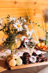 Sweet table with macarons, marshmallows and flowers in rustic interior.