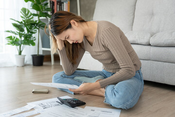 Stressed and headache asian woman with large bills or invoices no money to pay to expenses and...
