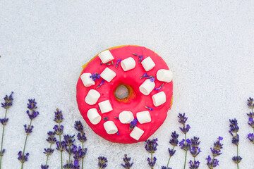 Colorful donut topped with mini marshmallows and lavender on a light background