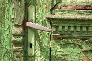 Close-up of a weathered green wooden door with peeling paint and a vintage metal handle, showcasing...