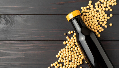 Artistic flatlay of soy sauce bottle surrounded by natural soybeans on dark wooden background

