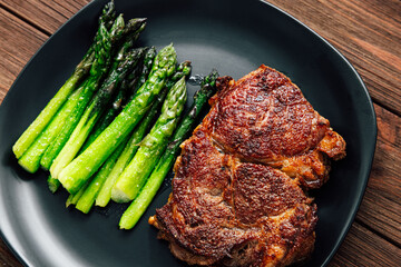 Delicious grilled steak with fresh asparagus on a black plate served on rustic wooden table