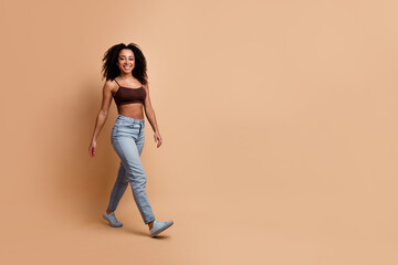 Graceful young woman walking confidently in casual attire with a smile and stylish hair against a...